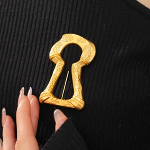 Detailed close-up of a vintage matte gold keyhole brooch on a black knit sweater