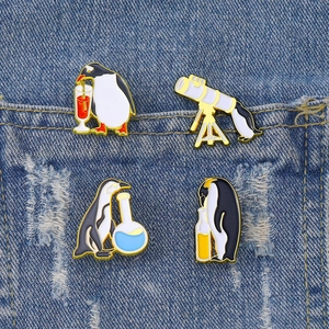 Set of four creative penguin enamel pins on blue denim pocket featuring celestial and lab themes