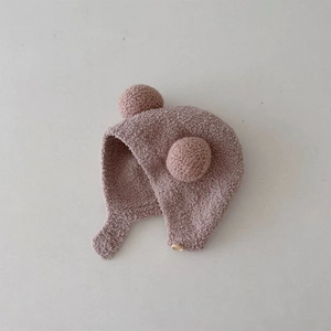 Detailed close-up of baby earflap hat in dusty pink featuring plush pom poms and button strap
