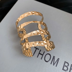 Detail of wide golden open bangle featuring hammered texture and multilayer wavy design