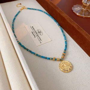 Macro detail of blue beaded necklace with a golden evil eye coin pendant and crystals