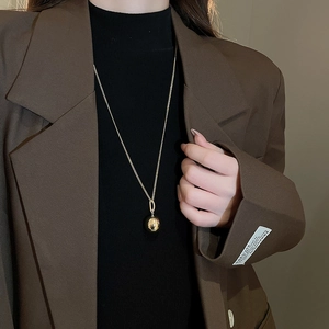 Detail of a minimalist gold ball pendant necklace worn over a dark brown blazer
