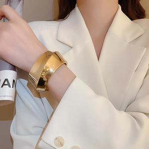Close-up of a minimalist wide gold cuff bracelet on a model wearing a white suit jacket