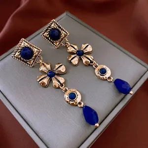 Detail view of vintage golden floral earrings with blue drop gemstones on red silk