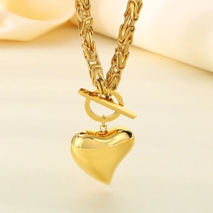 Close-up of golden heart pendant necklace with OT toggle clasp on beige silk fabric