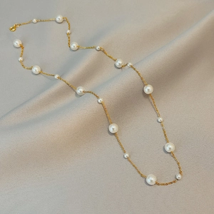 Elegant gold pearl necklace with alternating sizes on a grey fabric background