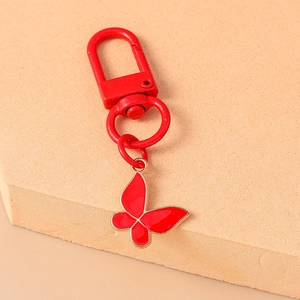 Detailed view of a red enamel butterfly keychain with metal carabiner on a beige platform