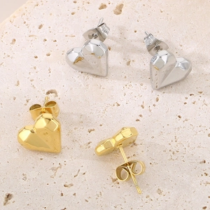 Detail of 3D heart stud earrings in gold and silver finish on textured stone background