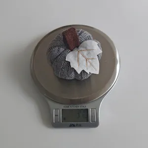 Detailed view of a grey knitted pumpkin decoration being weighed on a digital kitchen scale