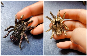Macro detail of vintage spider brooch featuring red and black rhinestones and safety pin clasp