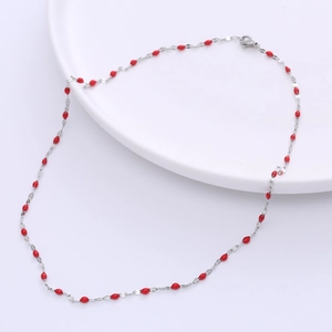 Detail of silver titanium steel necklace with small red enamel lip charms on white plate
