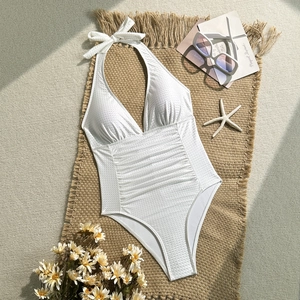 Detail eines weißen Neckholder-Badeanzugs mit Taillenraffung auf Strand-Hintergrund