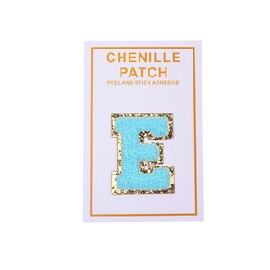 Macro detail of blue chenille letter E patch with gold sequins and peel-off adhesive