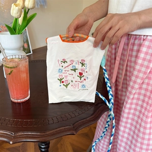 Détail de la broderie florale sur sac en toile blanche avec bandoulière tressée