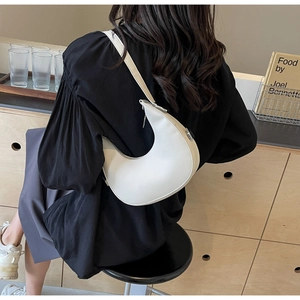 Detail view of a white crescent shoulder bag styled with an elegant black outfit