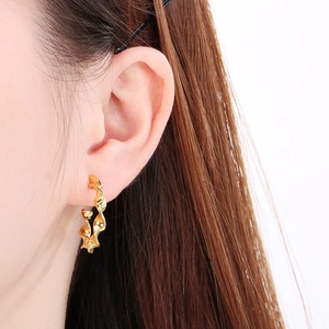 Close-up of a model wearing a golden twisted hoop earring in a minimalist Korean style