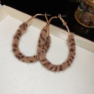 Détail de grandes créoles ovales dorées avec texture en fausse fourrure léopard