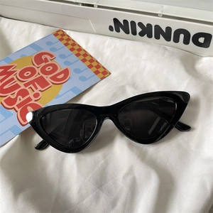 Detail of glossy black cat-eye sunglasses with dark lenses on a white fabric background