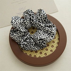 Detailed view of a soft black and white leopard print hair scrunchie on a wooden coaster