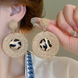Détail de boucles d'oreilles bohèmes en raphia tressé avec motifs léopard et métal doré
