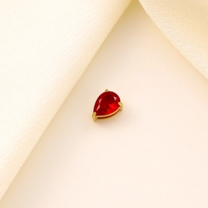 Macro shot of red pear-shaped zircon pendant with gold setting on beige silk fabric