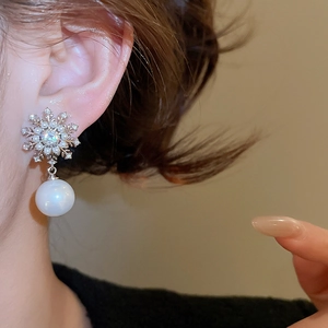 Macro view of snowflake stud earrings with sparkling zircon and a white pearl drop