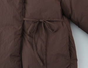 Detailed view of dark brown quilted jacket showing waist tie and fabric texture
