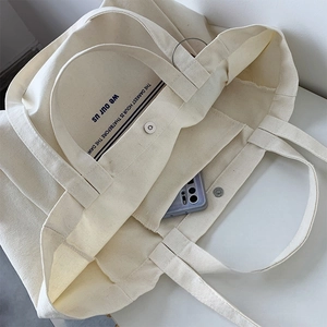 Detail of off-white canvas tote showing metal snap button and interior phone pocket