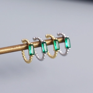 Detailed view of silver and gold cuff earrings with emerald zircon baguettes