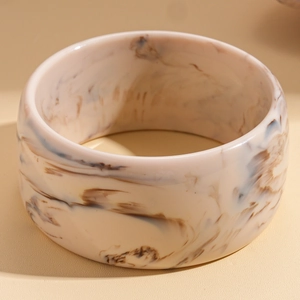 Macro shot of wide marble-patterned resin bangle with warm beige and brown tones