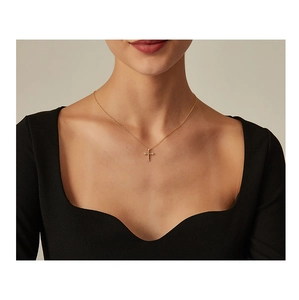 Close-up of a minimalist gold cross necklace with sparkling zircon stones on a model