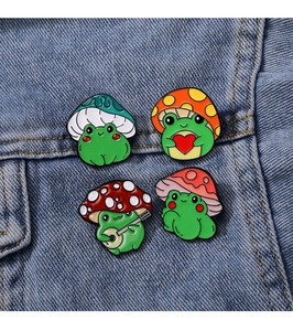 Detailed close-up of four cute frog enamel pins with mushroom hats on denim jacket