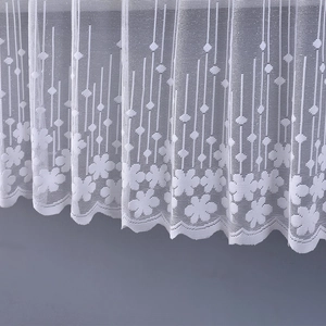 Detail of white lace cabinet curtain with floral daisy embroidery and scalloped edges
