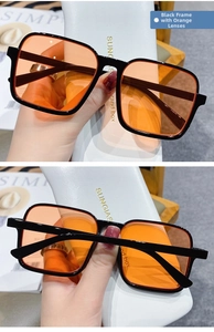 Detail view of square black frame sunglasses with orange lenses held over a case