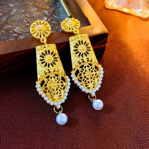 Macro shot of vintage style gold-tone earrings featuring white pearls and filigree detail
