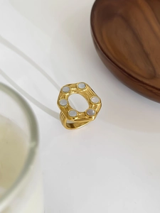 Detailed close-up of 18K gold-plated hexagonal ring with white shell inlays on table