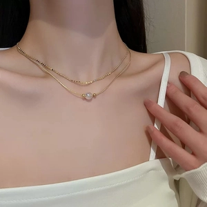 Detail view of a layered gold necklace featuring a pearl pendant on a delicate chain
