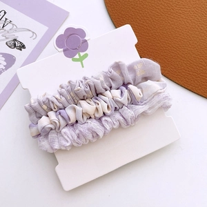 Détail de trois chouchous à fleurs violettes sur une carte de présentation Vogue Girl
