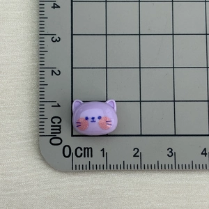 Mini purple resin cat charm with blue facial details shown on a measuring scale mat