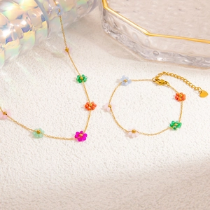 Detail of colorful beaded flower necklace and bracelet set on a textured white surface
