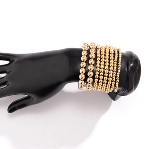 Detail of stacked gold beaded bracelets on a black mannequin hand for a minimalist look