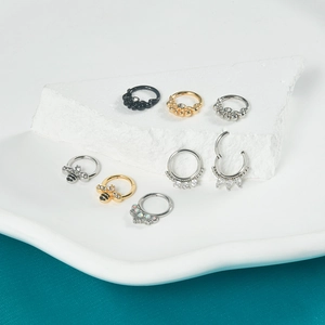 Collection of stainless steel bee and snake nose rings on white decorative stones