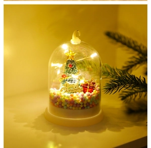Close-up of glowing glass cloche with green tree, red gift and Merry Christmas text