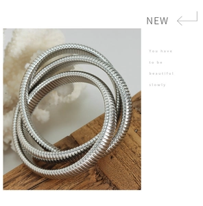 Detailed close-up of a silver triple-layered snake chain bracelet on a wooden texture
