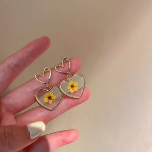 Gros plan détaillé de boucles d'oreilles cœur doré avec fleurs séchées jaunes en résine