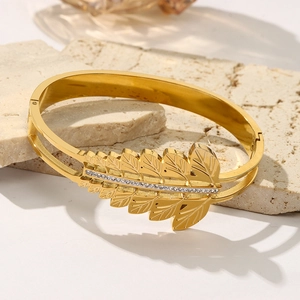 Gold leaf bangle with white zircon inlays and dual-layer band on a stone background