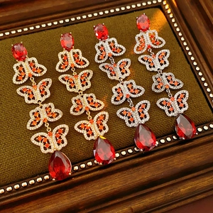 Détail de boucles d'oreilles papillon à pompons avec pierres rouges sur velours vert