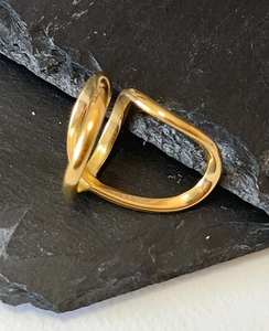 Detailed close-up of a gold irregular twisted ring with S.STEEL engraving on a black stone