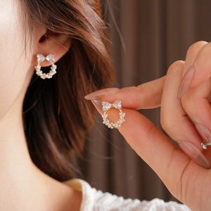 Détail de boucles d'oreilles nœud en zircon et mini perles dorées portées sur modèle