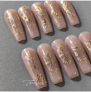 Macro detail of nude pink ballet press-on nails with golden floral patterns